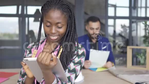 美国黑人妇女在平板电脑前看照片而男性设计师则在平板电脑中查看文件视频的预览图
