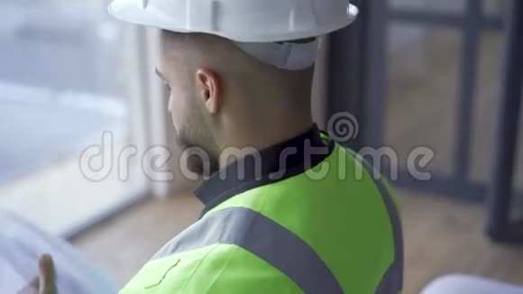 在头盔和绿色夹克阅读文件的胡须工人的特写具有建筑图纸的专业建筑商视频的预览图