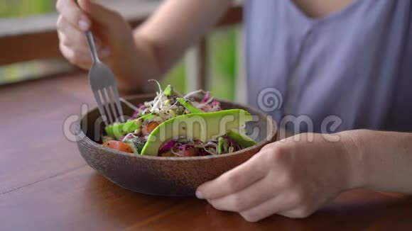 一个在热带咖啡馆里的年轻女人吃健康的素食沙拉素食概念慢镜头视频的预览图
