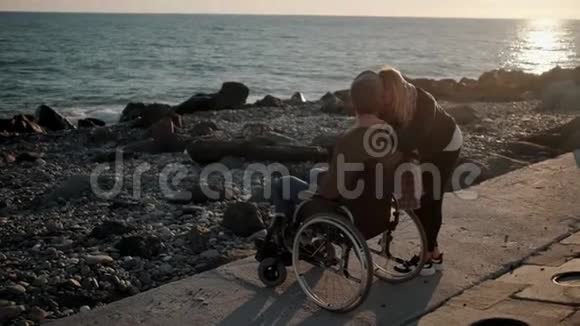 健康的女孩正在海上码头用轮椅拥抱生病的男友视频的预览图