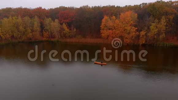 在金色的秋天人们漂浮在黄色的船上划着独木舟在河边靠近五颜六色的树视频的预览图