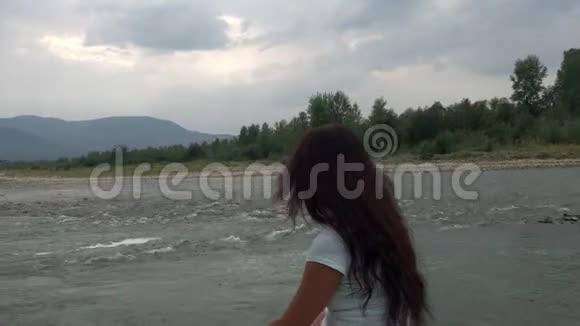 一个女孩坐在一条山河的岸边望向远方地平线上可以看到山脉视频的预览图