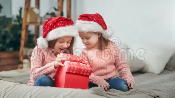 两个戴着圣诞帽的快乐女孩惊喜地打开了圣诞礼物盒充满了积极的情绪视频的预览图