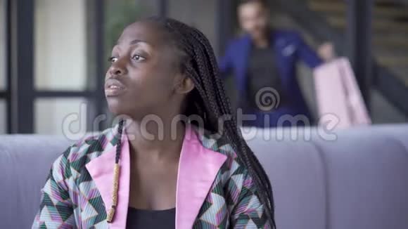 悲伤的非裔美国女人坐在沙发上看着远方穿着西装的帅哥从商店回来视频的预览图
