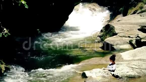 小女孩躺在石头上晒日光浴自然山河池塘与瀑布视频的预览图