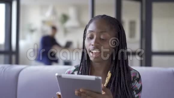 年轻漂亮的非裔美国女人梳着非洲辫子坐在家里用她的平板电脑工作女孩叫她视频的预览图