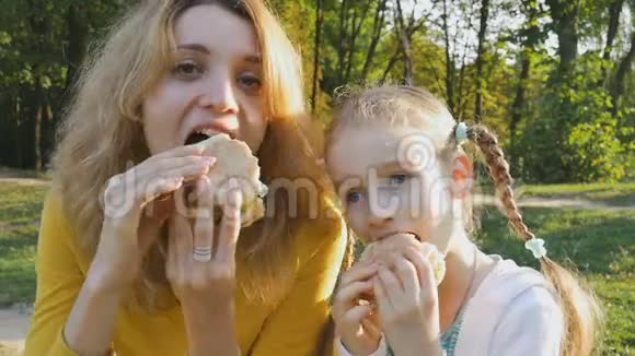公园里坐在长凳上吃快餐的年轻金发母亲和她的小女儿的特写照片视频的预览图