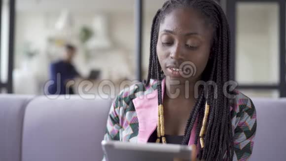 年轻漂亮的非裔美国女人皮肤有问题坐在家里用她的平板电脑工作室内休闲女孩视频的预览图