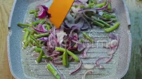 一只雌性手用木铲将洋葱和青豆放入锅中视频的预览图