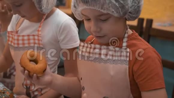 小男孩在烹饪学校做甜甜圈时舔手指穿着烹饪帽和围裙准备甜甜圈的男孩视频的预览图
