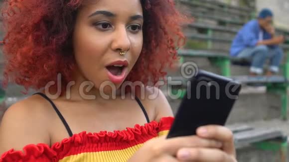 兴奋的红头发年轻女性带着鼻环在手机上看视频应用程序视频的预览图