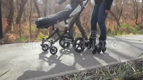 在秋天阳光明媚的天气里年轻的妈妈和爸爸正穿着旱冰鞋和他们的孩子在婴儿车里散步慢视野视频的预览图