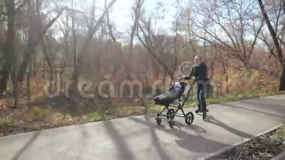 秋天一个年轻的家庭在一个早晨的城市公园里带着一个坐在滚轮上的靠边走路爸爸会耍花样慢动作视频的预览图