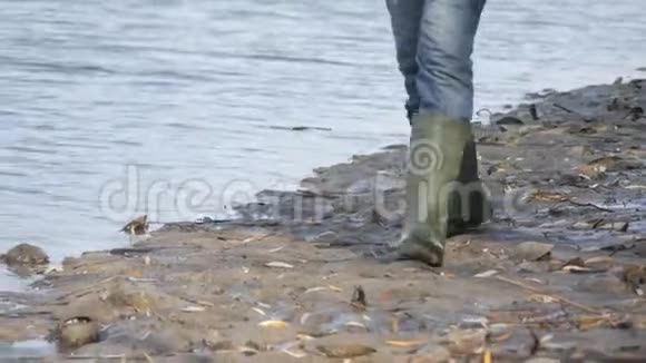 一个穿着绿色橡胶靴的渔夫正沿着水库的沼泽海岸散步视频的预览图