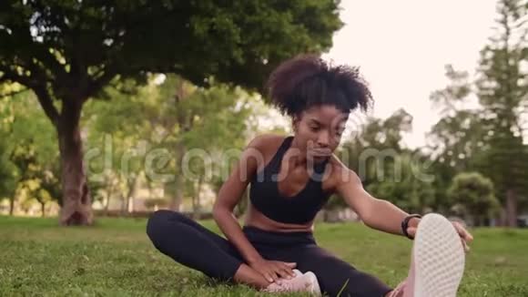 健康的年轻非洲裔美国妇女穿着黑色运动服在公园健身运动前伸展双腿视频的预览图