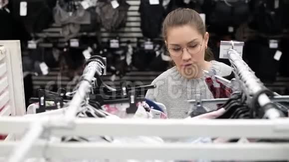 带眼镜的年轻女子正在超市里寻找合适的衣服视频的预览图