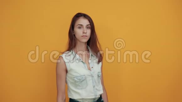 穿着蓝色牛仔衬衫的严格的白种人年轻女子在橙色的墙边视频的预览图