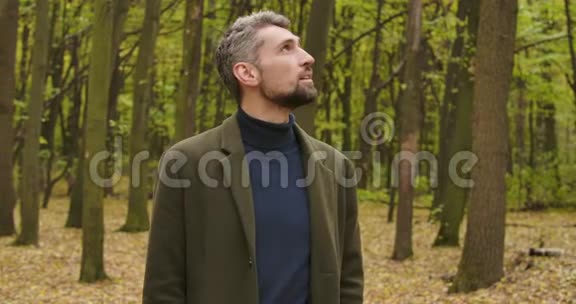 一个白发苍苍的白人男子的特写镜头站在森林里抬头看穿着休闲服装的男人享受着宁静视频的预览图