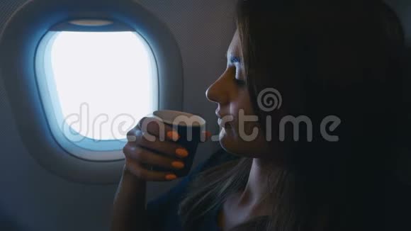 坐飞机旅行的女人年轻的女性旅行者在飞机上靠窗喝咖啡飞行视频的预览图