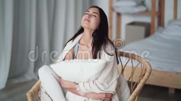 美丽的女人裹着格子呢坐在扶手椅上双手抱着枕头视频的预览图