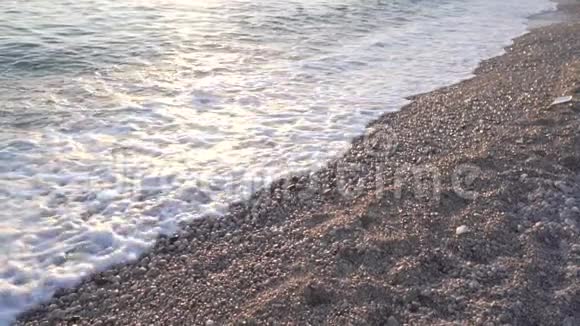 在阳光充足的沙砾海滩上特写了海浪的慢镜头日落日出时间白光海洋泡沫视频的预览图