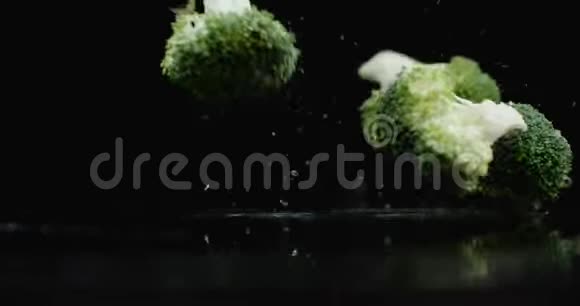 三个绿色的新鲜西兰花落在玻璃上溅起水花在黑暗的背景下缓慢地滴着水视频的预览图
