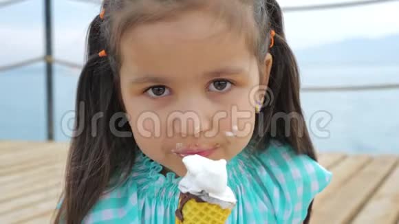小女孩在大海或海洋的背景上舔冰淇淋锥视频的预览图