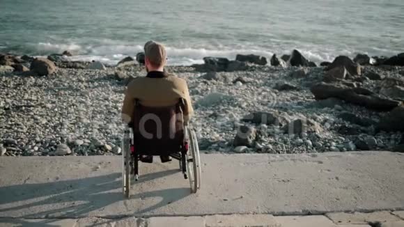 独自坐在轮椅上的男性乘客平静地坐在海岸上放松地后视视频的预览图