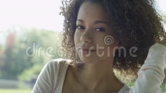 年轻美丽的混血女人卷发在一个绿色的公园里快乐地微笑视频的预览图