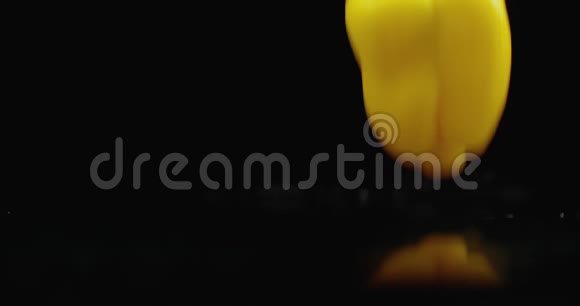 一个黄色的切钟胡椒落在玻璃上水在黑暗的背景上缓慢地飞溅视频的预览图