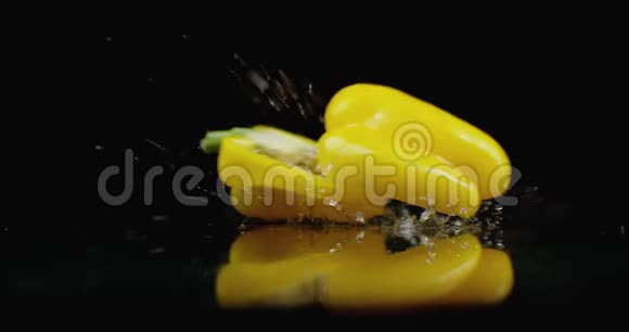 黄色的切钟胡椒落在玻璃上水在黑暗的背景上缓慢地飞溅视频的预览图