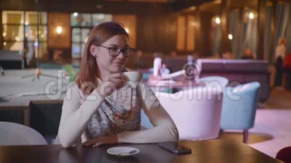 咖啡休息时间戴眼镜的迷人微笑的女人喜欢在咖啡馆放松喝着美味的咖啡看着相机视频的预览图