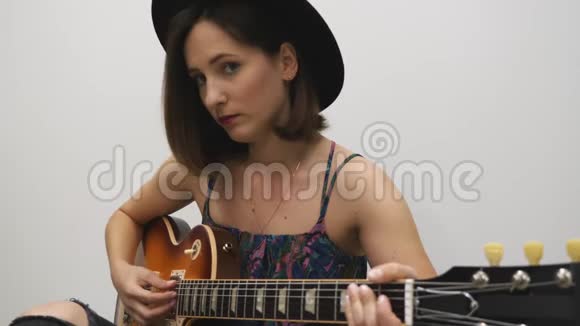 女人一边看电话一边练习弹吉他戴着吉他戴着帽子的年轻时髦女孩坐在地板上看着视频的预览图