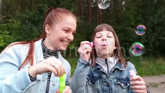一个年轻的女人和她的女儿在一个夏天的晚上母亲节在公园里吹泡泡家庭关系视频的预览图