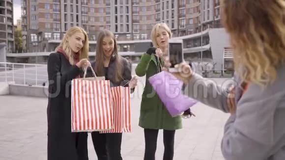 三个带着购物袋的快乐女孩摆姿势给第四个朋友拍照城里四个时尚女人视频的预览图
