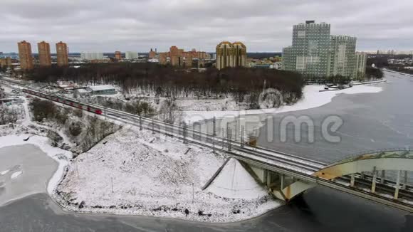 航景飞行跟踪一列移动轨道列车在结冰的河流上行驶的桥梁视频的预览图