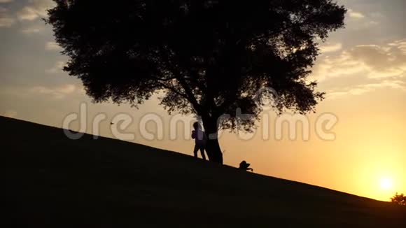 日落时分女孩在大树旁缓慢地上坡视频的预览图