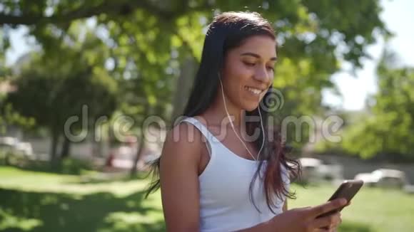 漂亮的黑发混血女听着耳机里的音乐用手机发短信和朋友聊天视频的预览图