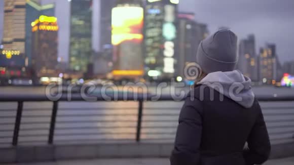 一个穿着黑色夹克和帽子的年轻女孩看着瓦伊坦海滨的上海景色视频的预览图