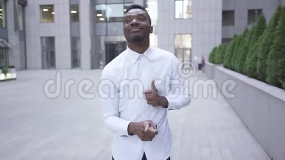 满意的非裔美国人穿着白色衬衫在城市街道上的现代商务中心前跳舞男性视频的预览图