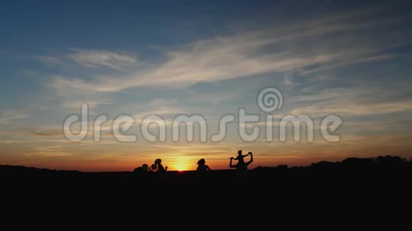 日落时在草地上奔跑的家庭剪影视频的预览图
