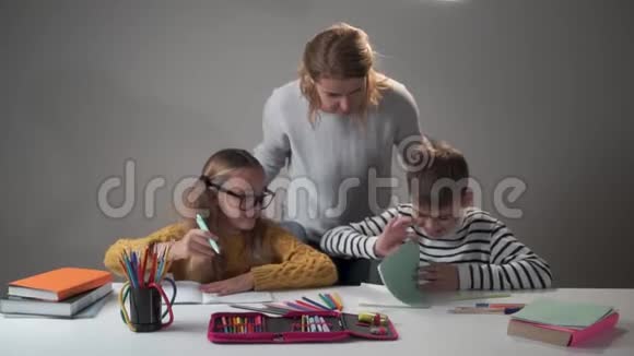 年轻的白种人女教师给孩子任务戴眼镜的漂亮女孩和她的男同学坐在视频的预览图