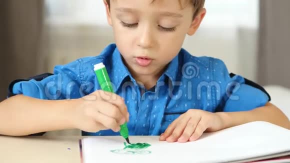 一个小男孩想象着坐在桌子旁画画幼儿画鲜艳的毡笔视频的预览图