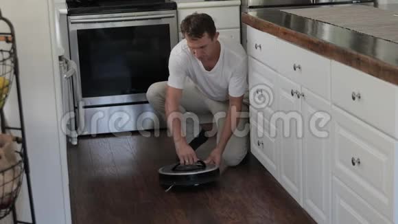 成年男子正在厨房地板上放置圆形机器人吸尘器切换视频的预览图