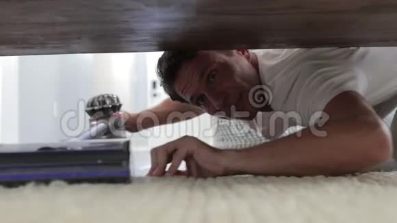年轻人用吸尘器打扫躺在地板上的床下的地板视频的预览图
