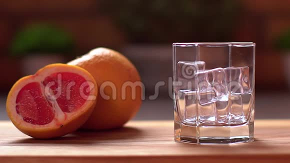 新鲜葡萄柚汁倒入透明玻璃加冰把葡萄水果切成薄片放在桌子上健康生活方式视频的预览图