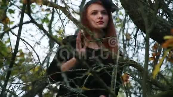 一个穿着黑袍红头发像巫婆一样的女人穿过灌木丛和干树枝视频的预览图