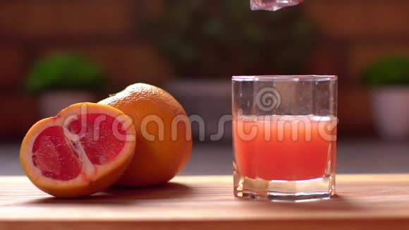 一个面目全非的人把冰块扔进一个装有新鲜柑橘葡萄柚汁的杯子里视频的预览图