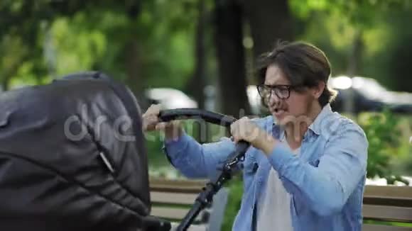 疯狂的年轻父亲紧张地在城市公园摇摆婴儿车视频的预览图