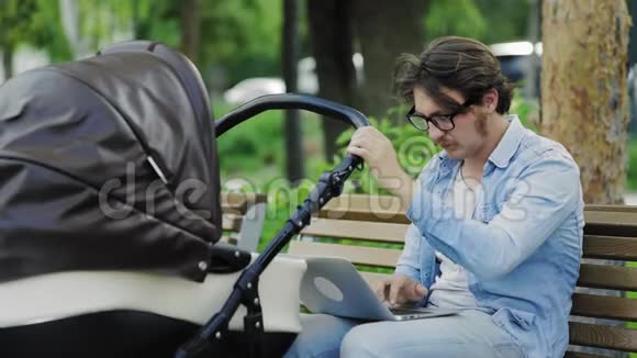 现代年轻爸爸工作笔记本电脑和摇摆婴儿车多任务生活方式视频的预览图